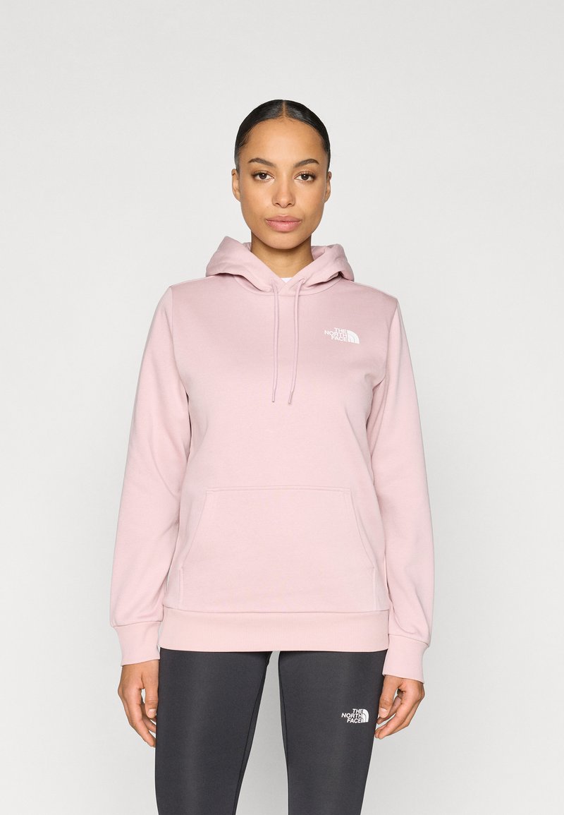 Light pink hooded sweatshirt made of soft fabric, featuring a front pocket and white logo on the chest, paired with dark gray leggings.