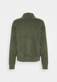 Olivgrüne, gerippte Kordjacke mit langen Ärmeln und Manschetten, geradem Saum und Stehkragen, von hinten auf weißem Hintergrund gezeigt.