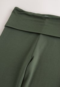 Olivgrüne Leggings mit hohem, umgeschlagenem Bund. Hergestellt aus glattem, dehnbarem Stoff. Verfügt über eine schlanke, stromlinienförmige Passform ohne sichtbare Nähte.