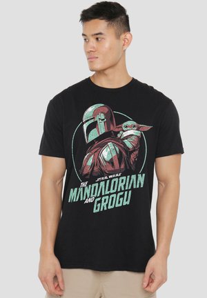 Mann trägt schwarzes T-Shirt mit Star Wars-Charakteren The Mandalorian und Grogu in stilisierter Grafik mit Text darunter.