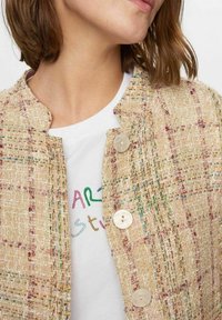 Veste beige tissée avec une finition texturée, présentant des fils multicolores, un col rond, et cinq boutons circulaires sur le devant.
