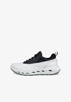 Nizka tekaška superga s črnim zgornjim delom in belim podplatom, z belim podplatom z geometrijskimi izrezi in zanko za poteg na peti.