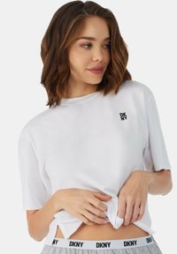 Witte katoenen t-shirt met korte mouwen en een ronde hals, voorzien van een klein zwart DKNY-logo op de borst, gecombineerd met grijze bottoms met elastische tailleband.
