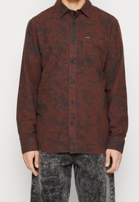 Röd och svart mönstrad långärmad skjorta med knappslutning fram, en bröstficka och en avslappnad passform. Lättviktsmaterial med en mjuk textur.