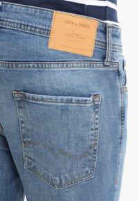 Ljusblå denimjeans har en läderloggopatch märkt "JACK & JONES" på midjebandet, med en lätt sliten struktur och rundad sömnad.