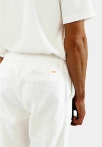 Weiße Leinenhose mit elastischem Bund und Gesäßtasche, kombiniert mit einem strukturierten weißen Kurzarmoberteil. Minimalistisches Design.