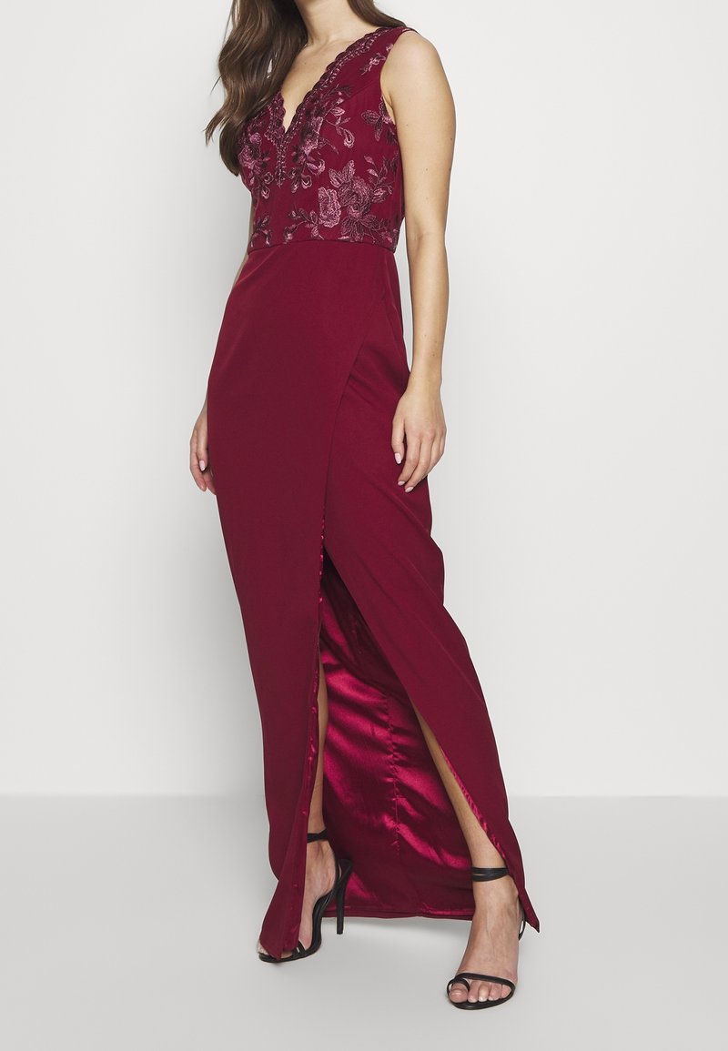 Burgundykvällklänning med djup V-ringning, dekorerad bodice och sidoklyvning. Tillverkad av ett slätt tyg med en blank innertyg.