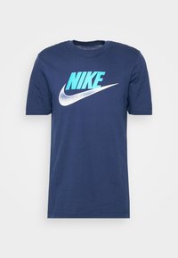 Marinblå t-shirt i bomull med en stor turkos "NIKE"-grafik och en vit swoosh-logotyp på framsidan. Korta ärmar, rundad halsringning.