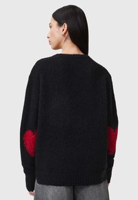 Schwarzer Strickpullover mit strukturiertem Finish, versehen mit großen roten Herzmotiven an jedem Ärmel, Rundhalsausschnitt und geripptem Saum.