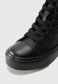 Black high-top sneaker featuring a smooth leather upper, rubber toe cap, black laces, and textured rubber sole with circular pattern.