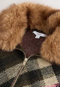 Mantel mit Kunstpelzkragen und Reißverschluss. Brauner Pelz, gemustertes Wollstoff in Erdtönen und eine rosa karierte Innenfutter. Goldfarbene Hardware-Akzente.