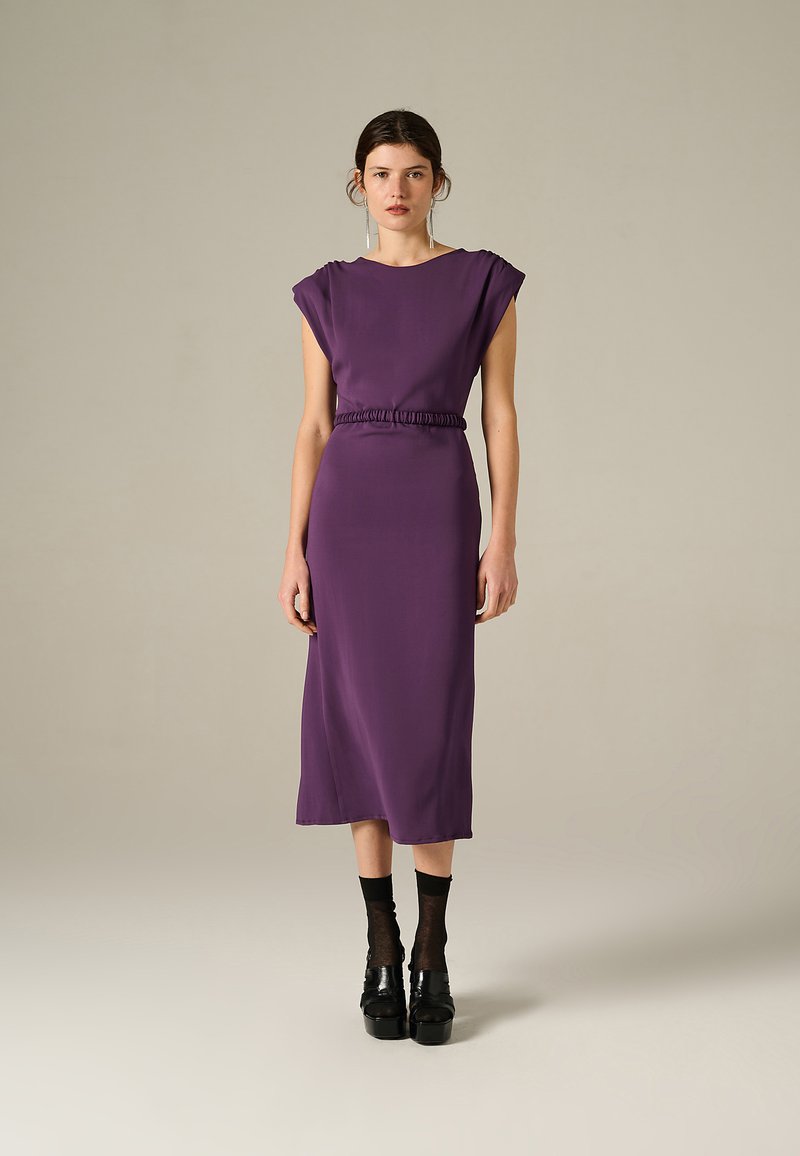 Abito midi viola con una vestibilità rilassata, vita arricciata e maniche larghe. Realizzato in un tessuto liscio, abbinato a calze nere e scarpe con zeppa.