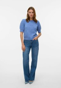 Pull en maille bleu clair avec des manches courtes bouffantes, associé à un jean bleu taille haute et des escarpins bleu à bout pointu.