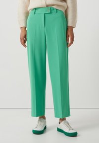 Mintgröna skräddarsydda byxor med raka ben, två frambutiker och en mjuk textur, stylade med vita sneakers med gröna accent.