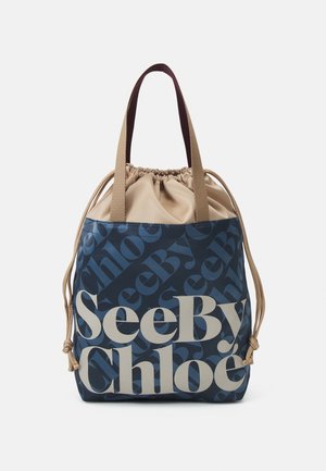 Niebiesko-beżowa torba typu tote See By Chloé z zamknięciem na sznurek i dwoma beżowymi uchwytami na białym tle.