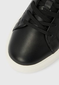 Μαύρο δερμάτινο αθλητικό παπούτσι με υφή στην επιφάνεια, διαθέτει μαύρα κορδόνια, λευκή λαστιχένια σόλα και στρογγυλεμένο σχέδιο μύτης.