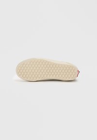 Såle av en sneakers, beige gummi med et teksturert diamantmønster og en rød aksent på hælen. Ren, minimalistisk design.