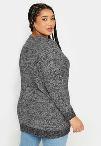 Långärmad tröja i svart och grå stickad tyg. Har en avslappnad passform, rund halsringning och ribbade ärmslut. Mjuk textur med subtilt mönster.