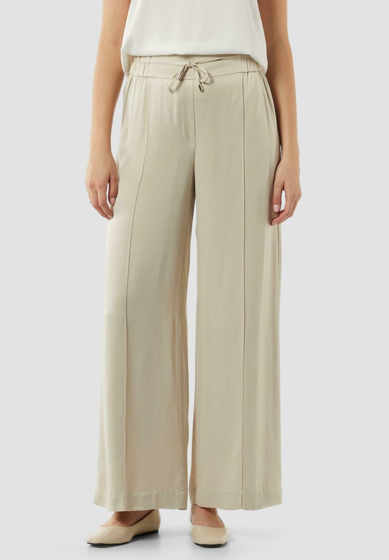 Beige weit geschnittene Hose mit elastischem Bund und Kordelzug, ausgestattet mit seitlichen Taschen und aus glattem, leichtem Stoff.