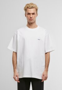 Hvit, oversized bomull t-skjorte med korte ermer og rund hals. Har en liten blå logo på brystet og en avslappet passform.