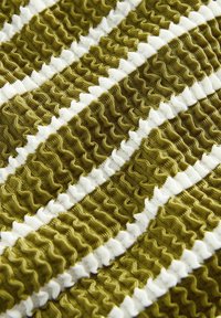 Texturerad tyg med olivgrön och vit vågformade ränder, med växlande volangmönster och släta sektioner för extra detalj.