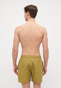 Shorts de bain pour hommes en vert olive, confectionnés dans un tissu léger, dotés d'une taille élastique et d'une poche arrière avec rabat.