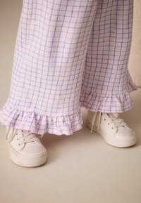 Ružové a biele kárované nohavice s volánikovými manžetami v kombinácii s bielymi plátennými teniskami s okrúhlou špičkou a perforovanými bočnými panelmi.