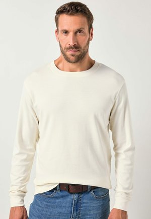 Camisa de manga larga color crema hecha de una tela suave, con un escote redondo y puños ajustados, combinada con jeans azules y un cinturón marrón.