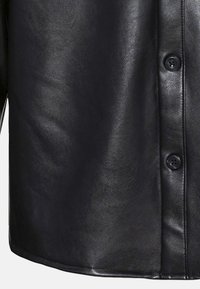 Chemise en cuir noire avec une texture lisse, dotée d'une fermeture à boutons à l'avant et d'un ourlet arrondi. Les détails incluent six boutons et une finition élégante.