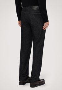 Pantalones de mezclilla oscura con corte recto, que cuentan con un parche de cuero en la cintura y sutiles detalles de costura en los bolsillos traseros.