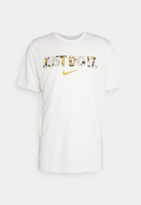 Biała bawełniana koszulka z krótkim rękawem z napisem "JUST DO IT" w stylu wykroju, z złotym logo Nike pod spodem. Okrągły dekolt.