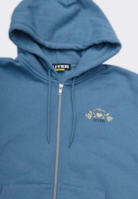 Felpa blu con zip e texture morbida. Presenta un logo floreale dorato e una tasca frontale a marsupio. Cappuccio regolabile con lacci.