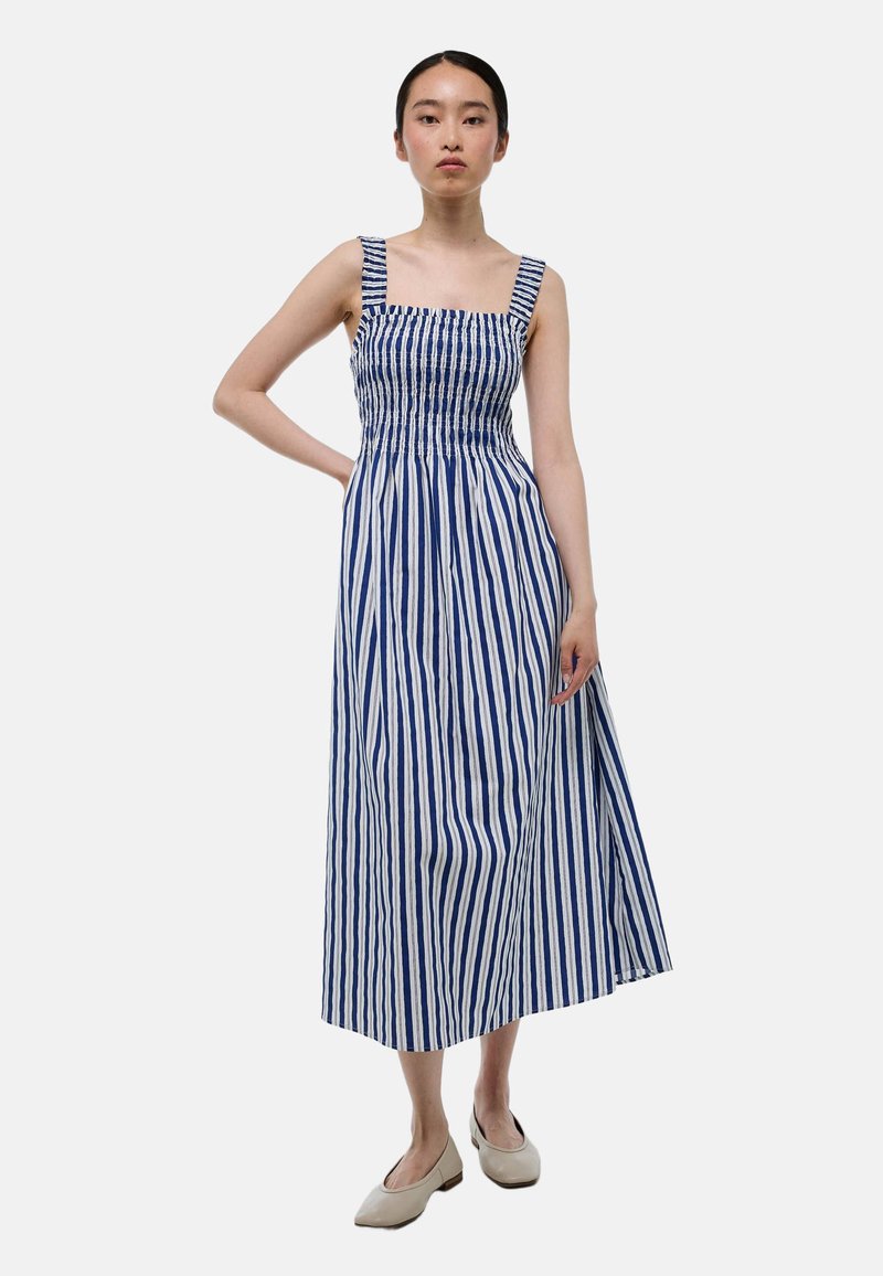 Robe maxi rayée bleue et blanche avec un corsage smocké, décolleté carré et larges bretelles. Tissu lisse avec une silhouette décontractée.