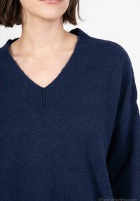 Pull en tricot bleu marine à décolleté en V, avec une texture douce et des coutures discrètes. Le design présente des manches larges et une coupe décontractée.