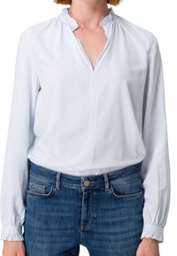 Helles, blau gestreiftes Blusenshirt mit gerafftem Kragen, langen Ärmeln und elastischen Bündchen, kombiniert mit blauen Jeans aus Denim. Einfaches Design.