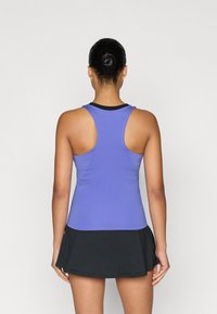 Μωβ αθλητική φανέλα με σχέδιο racerback, συνδυασμένη με μαύρη φούστα με σκίσιμο. Λεπτή υφή, εφαρμοστή στο πάνω μέρος και φαρδιά στην άκρη.