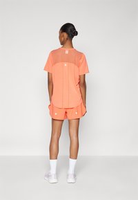 Top deportivo de coral de manga corta con espalda de malla, combinado con pantalones cortos coral con acentos blancos. Textura suave y corte relajado.