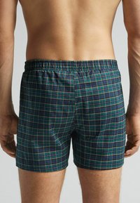 Pánské boxerky v tmavě zeleném a námořnickém kostkovaném vzoru, s elastickým páskem. Materiál je lehký a hladký.