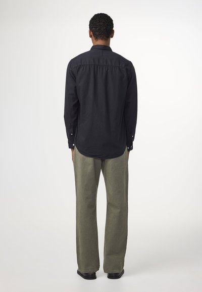 Chemise noire à manches longues avec un ourlet arrondi, assortie à un pantalon léger olive clair décontracté et des chaussures noires, vue de dos.