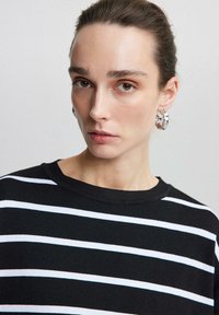 Svart-och-vit randig tröja med rund halsringning, strukturerad tyg och långa ärmar. Modellen bär iögonfallande hängande örhängen.