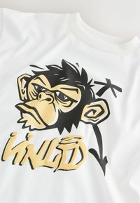 Weißes Baumwoll-T-Shirt mit einem grafischen Design eines stilisierten Affengesichts in Schwarz und Gold und dem Text "UNLD" in fetter Schrift.