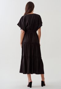 Černé maxi šaty ve vrstvách s krátkými volánovými rukávy a páskem v pase. Mají měkkou látku a splývavý střih. Jednoduchý design.