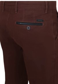 Braune Baumwollhosen mit einer Gesäßtasche in Marineblau und Knopfverschluss. Glatte Textur mit kontrastierendem Stichdetail.