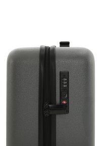 Hard-shell suitcase in textured dark gray, featuring a double zipper, combination lock, and a top carry handle. Slim, rectangular design.
