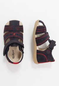 Sandalias de cuero marinas con costuras rojas, diseño abierto, correas de velcro y suelas de goma beige. Presentan una plantilla acolchada.