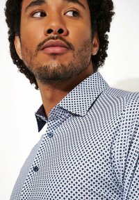 Lange mouwen knoopshirt met een blauw stippenpatroon op een witte achtergrond, met een contrasterende kraag en blauwe knopen.