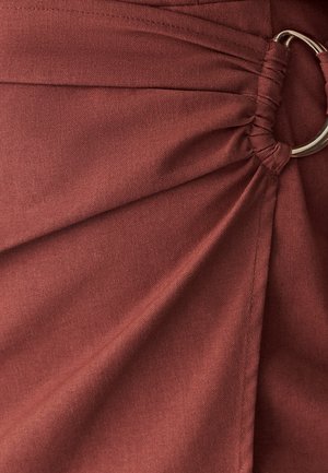 Rust-colored fabric with a smooth texture, featuring gathered pleats and a circular metal ring accent, creating a structured drape.