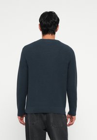 Dark blue knitted sweater with a ribbed texture, round neckline, and long sleeves. Hem and cuffs are slightly fitted, providing structured shape.