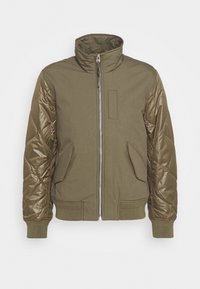 Giacca verde oliva con maniche in satin trapuntato, colletto alto, zip frontale, tasche con pattina e polsini e vita a coste.