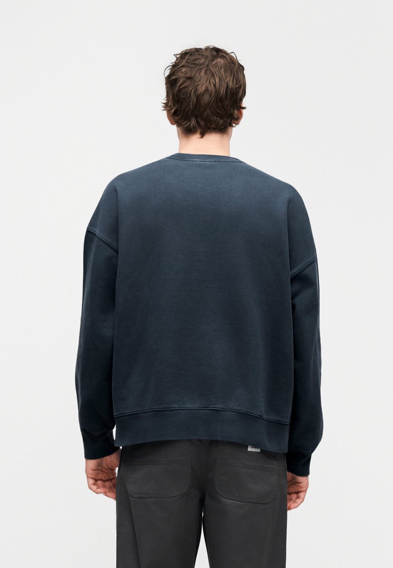 Felpa blu navy con scollo tondo, spalle scese e polsini a costine. Tessuto liscio con una vestibilità rilassata e dettagli di cuciture visibili.